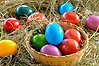 I en korg omgiven av hö ligger massor av färgglada ägg.