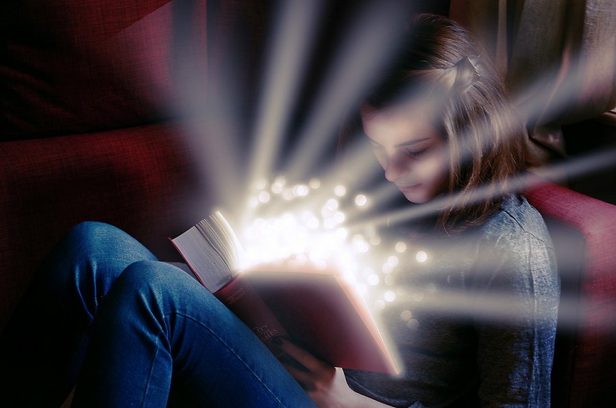 Foto på en flicka som sitter uppkrupen i en soffa och läser i en bok. Ur boken strålar ljus och glitter.