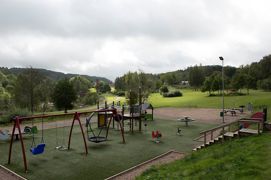 Foto på lekplatsen vi örekilsälven. Lekplatsen har ett underlag av konstgräs och flera olika lekredskap som gungställning, rutschkana och klätterställning.