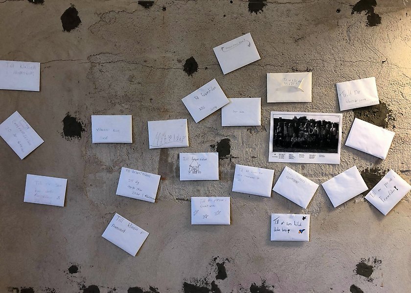 Foto på en betongvägg där det sitter 20 små brev och ett klassfoto.