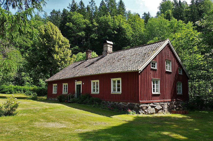 Foto på ett falurött hus med vita fönster och stengrund. Runt om huset växer träd och framför är en välklippt gräsmatta.