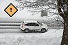 Bil som kör på snöig väg och en symbol för orange vädervarning