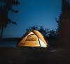 Ett upplyst tält på natten vid en sjö med en stjärnklar himmel.