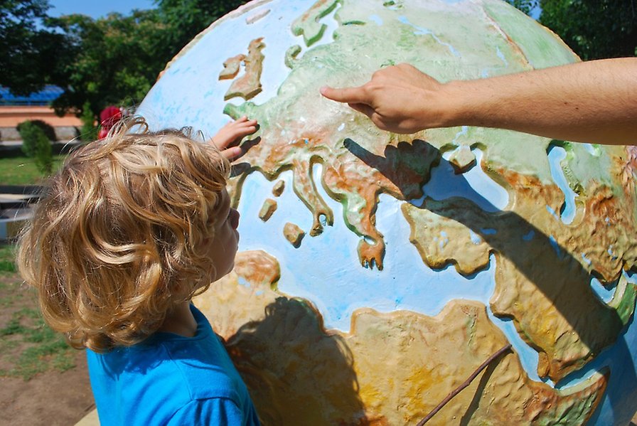 Bild på ett barn och en vuxen pekar på en jordglob.