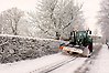 En traktor med plogblad kör på en väg och plogar bort snö.