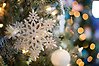 Foto på en vit och glittrig prydnad formad som en snöflinga som hänger i en julgran.