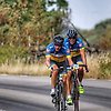 Foto på två personer som cyklar på en landsväg. De har på sig cykelhjälm och blå-gula träningskläder.