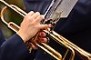 Foto på händer som spelar på en trumpet, naglarna är målade. På trumpeten sitter ett litet notställ.