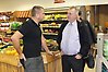 Bild på Sven-Erik Bucht och Kent Johansson som står och pratar med varandra framför fruktdisken inne i Kents butik.