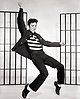 Svartvit bild på Elvis Presley. Elvis står på en sen och gör ett danssteg samtidigt som han sjunger.