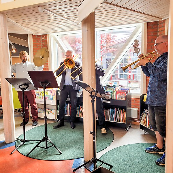 Musiker som spelar blåsinstrument och cymbaler i ett bibliotek.