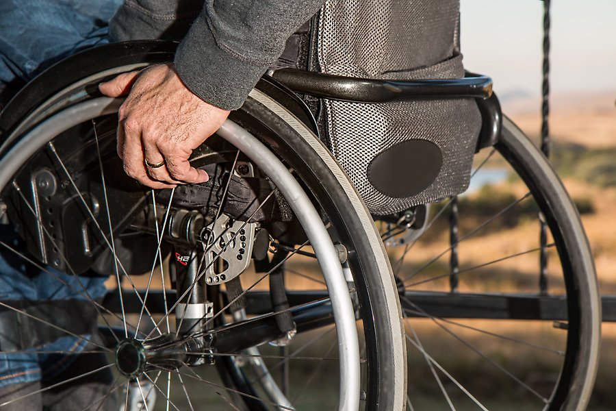 Närbild på sidan av en rullstol. Man ser en hand som rullar hjulet.
