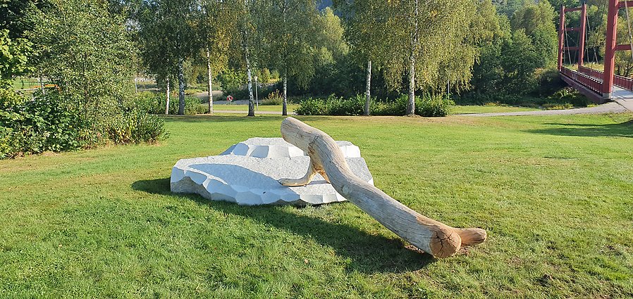 En stor sten som liknar ett isflak med en stor stock som vilar på den. Stocken är utformad så den liknar en säl med de främre fenorna ståendes på stenen. Konstverket är placerad i en park med lummiga träd och buskar.