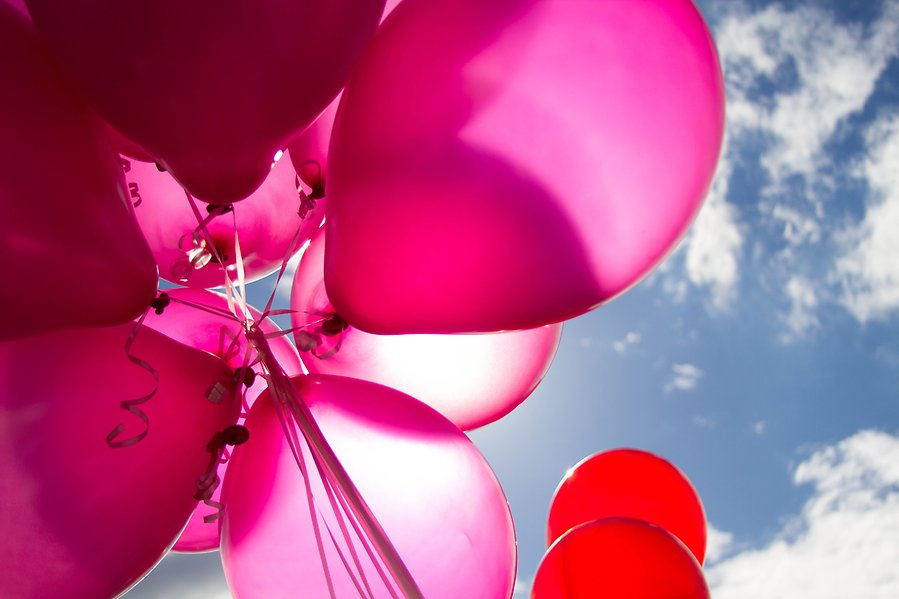 Ett knippe rosa ballonger som hålls upp mot himlen. Solen skiner bakom ballongerna.