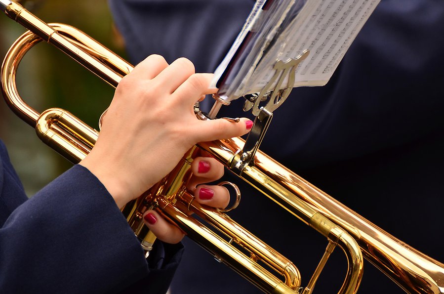 Foto på händer med röda naglar som spelar på en trumpet. På trumpeten sitter ett litet notställ med noter på.