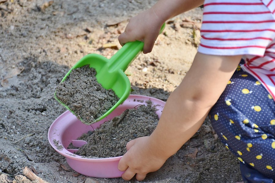 Närbild på ett barns händer som som gräver i en sandlåda med en spade. 