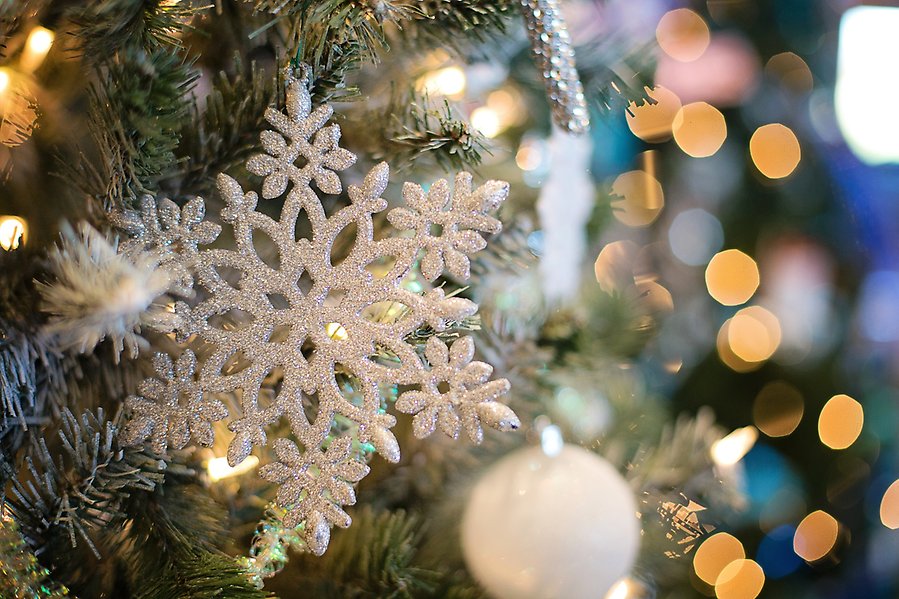 Foto på en vit och glittrig prydnad formad som en snöflinga som hänger i en julgran.