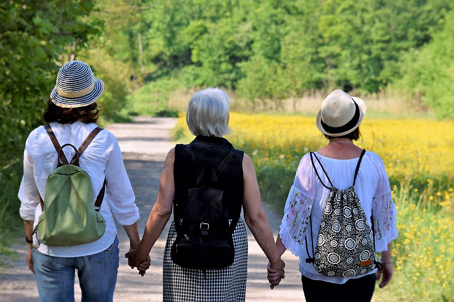 Foto på tre kvinnor i olika åldrar som går hand i hand på en grusväg.