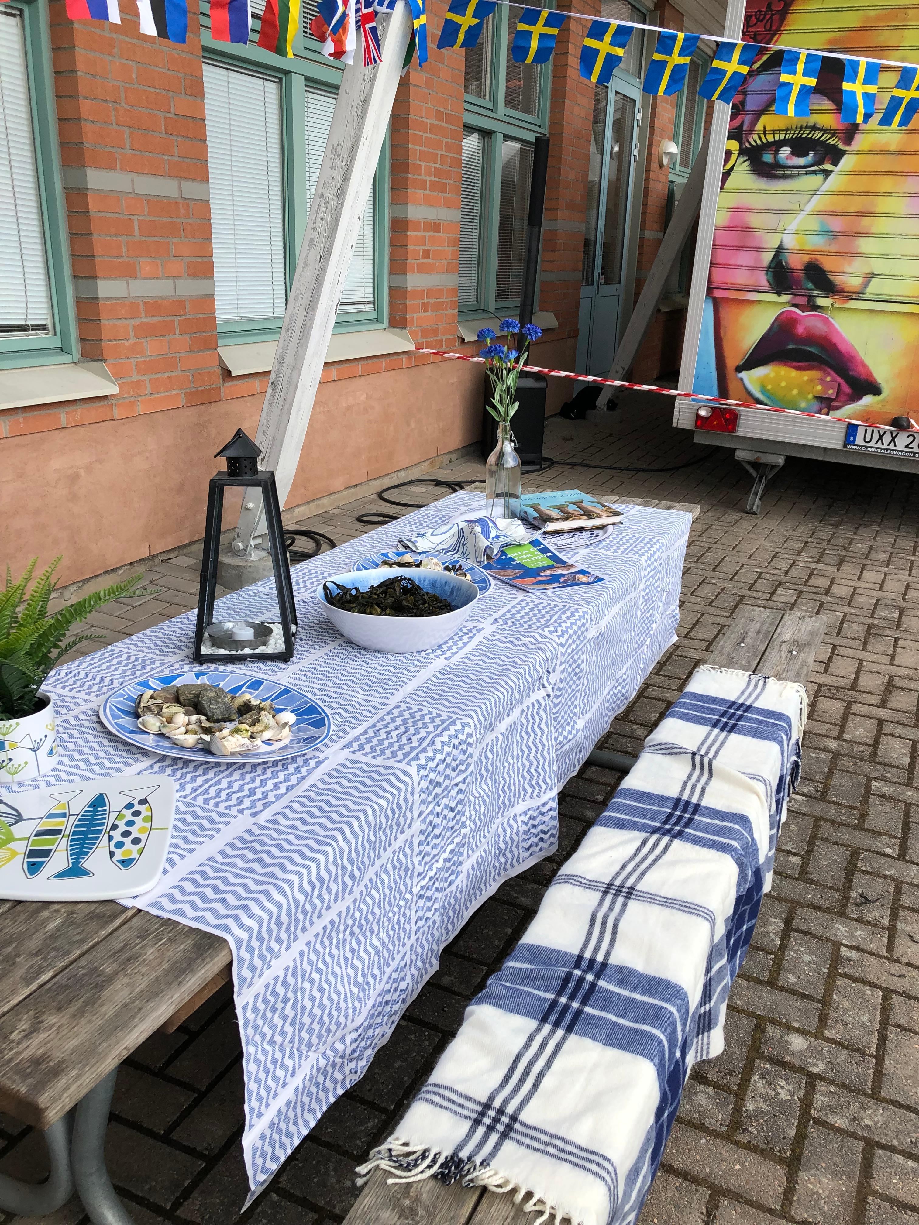 Ett långbord med somrig duk. På bordet står fat med olika små maträtter. På sittbrädorna ligger en filt.