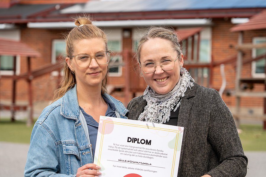 Två kvinnor som står utomhus med ett diplom.