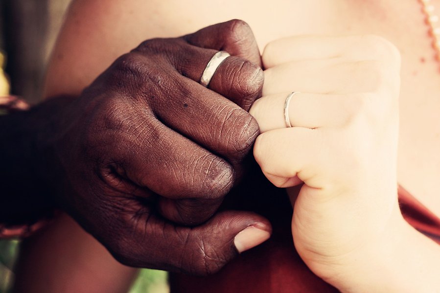 Foto på två personer med varsin vigselring av vitt guld. Personerna knyter sina händer som ringarna sitter på och håller dem mot varandra.