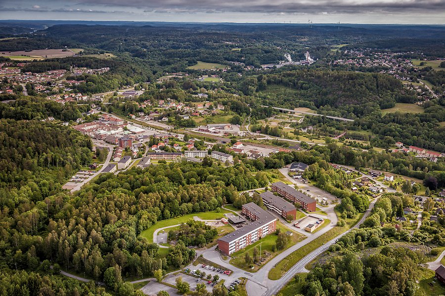 Flygfoto över en del av ett samhälle. Mellan skogspartier ses bland annat flerfamiljshus.