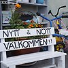 Bild på en vit träbänk som det står "Nytt & Nött" på i svart text. I bakgrunden syns orange blommor och en blå cykel. 