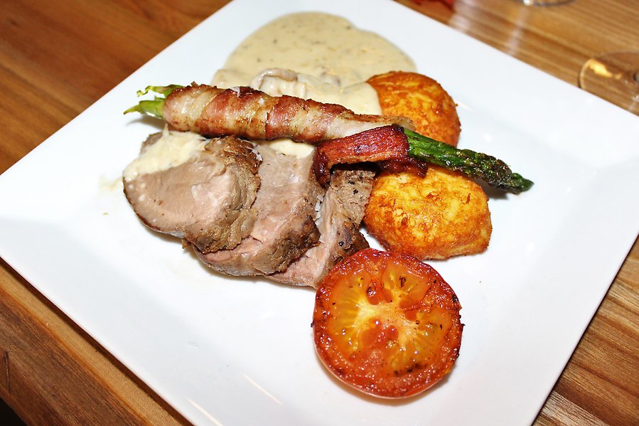 Bild på en vit tallrik med köttbitar, gräddsås, baconinlindad sparris, grillad tomat och potatis.