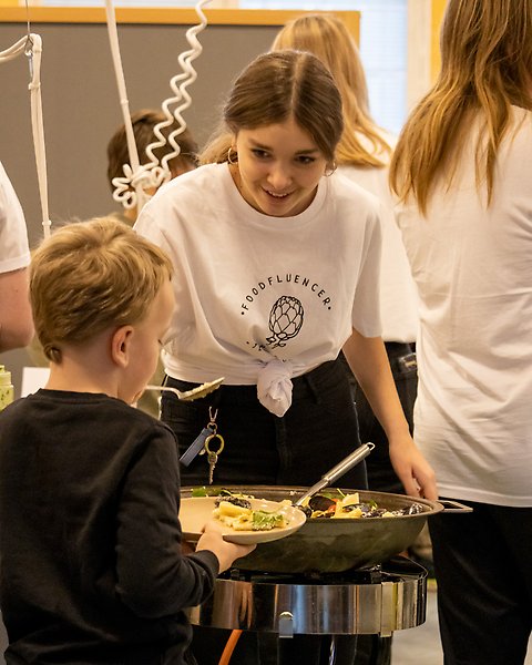 En ungdom som serverar en yngre elev i matsalen