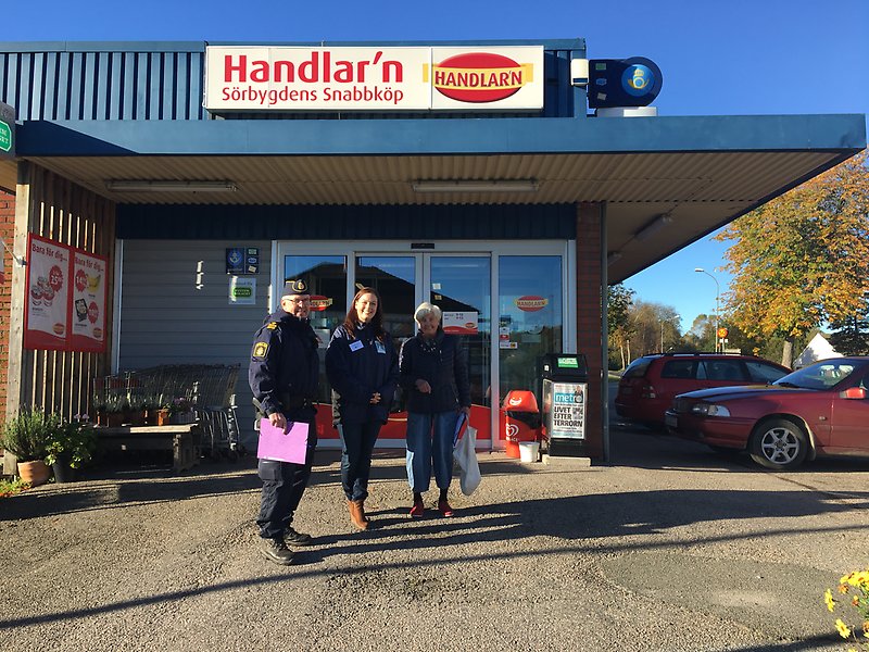 Tre personer står utanför en mataffär med skylten "Handlar'n" på.