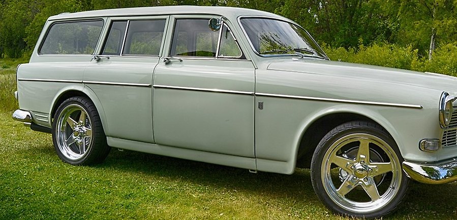 En bil av äldre kombimodell står parkerad på grönt gräs. Bilen har en ljus grågrön färg.
